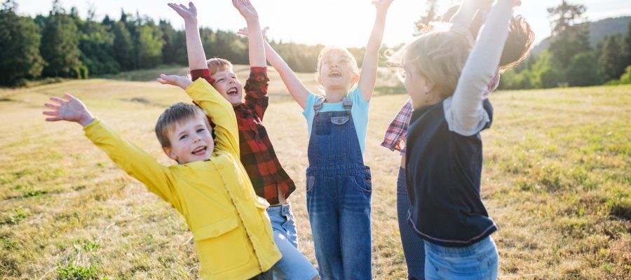 Portrait of group of school children standing on field trip in nature, playing.